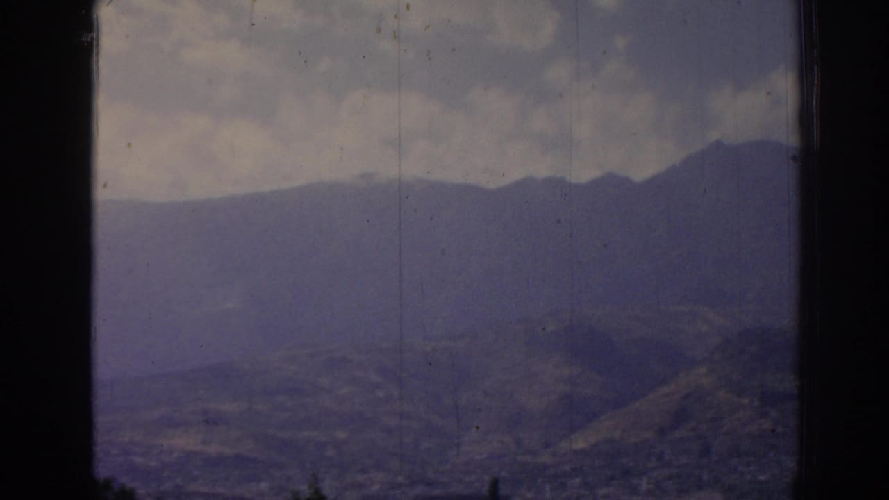 1962 8mm view near Izmir, Turkey, showing a distant mountain ridge, hazy hills, and clouds framed by a dark window edge.
