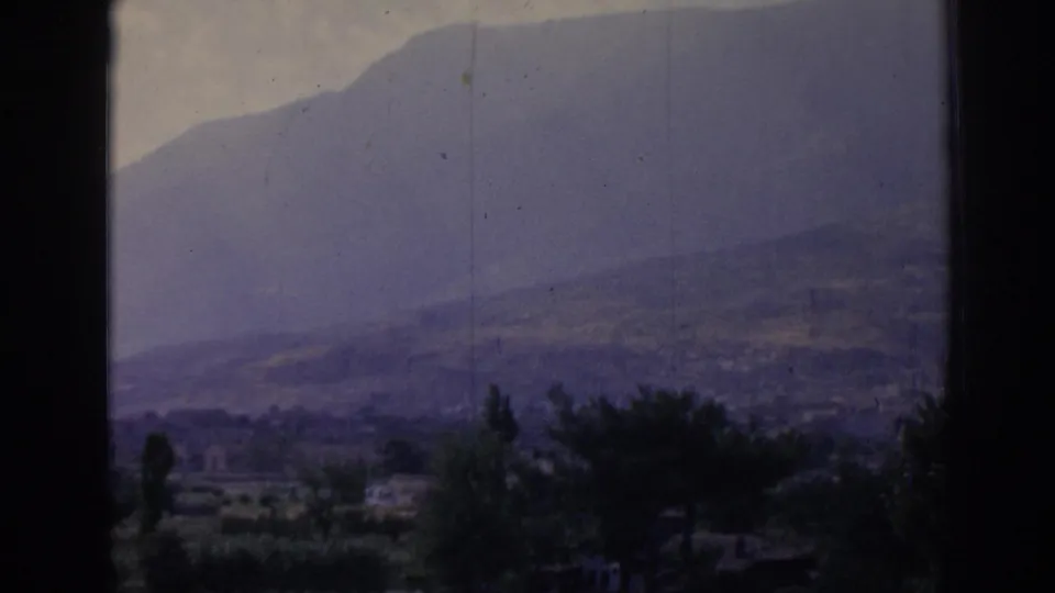 1962 8mm landscape near Izmir showing a hazy hillside above fields and trees, framed by dark edges and visible film wear.