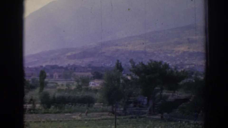 1962 home-movie view near Izmir with fields, trees, a few low buildings, and a broad hillside in soft faded color.