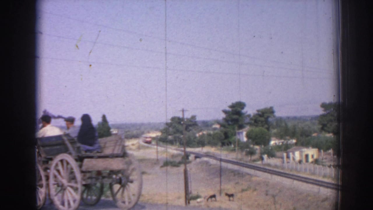Horse-drawn cart with riders beside a road and rail tracks.