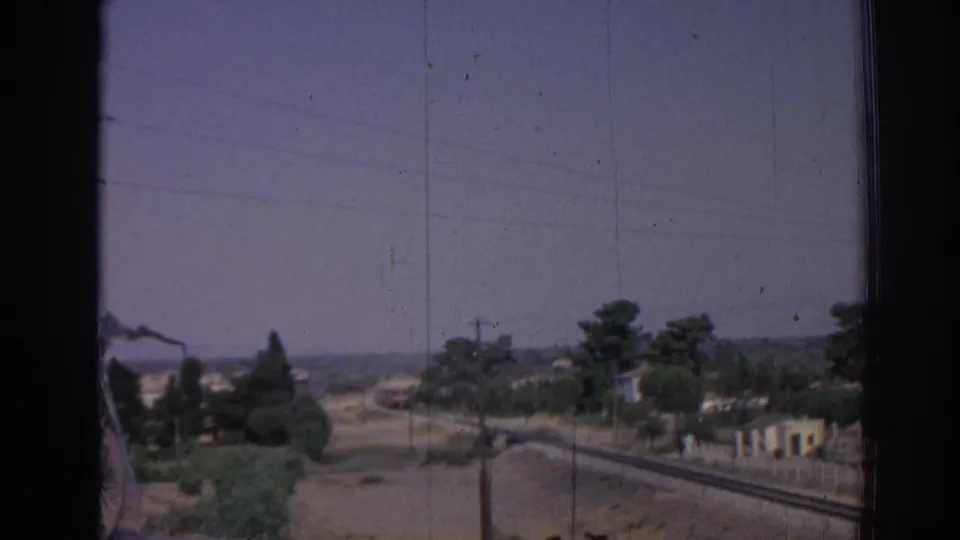 Izmir roadside landscape in 1962 with rail tracks, trees, low buildings, and a train visible in the distance.