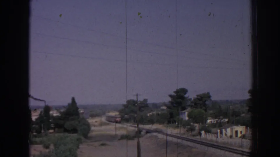 1962 Izmir view of rail tracks and a road running past trees and small buildings toward a distant train.