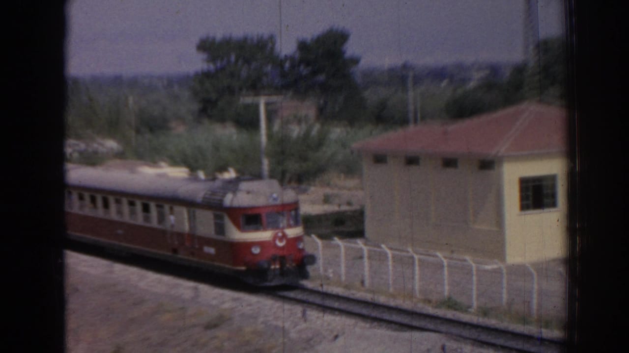 Red-and-cream train approaches beside a small yellow building.