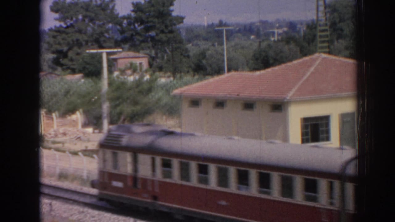 Red-and-cream passenger train passing a small yellow station building with a red-tiled roof.