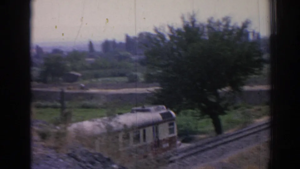 1962 Izmir-area frame with a red-and-cream train traveling through a rural trackside scene with trees and fields.