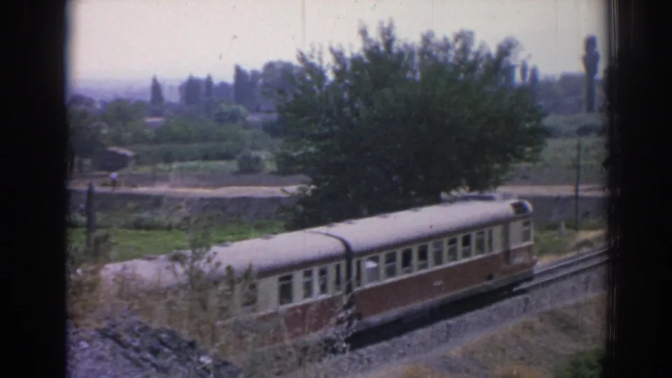 1962 Izmir-area home-movie view of a passenger rail car moving past trees, fields, and trackside vegetation.