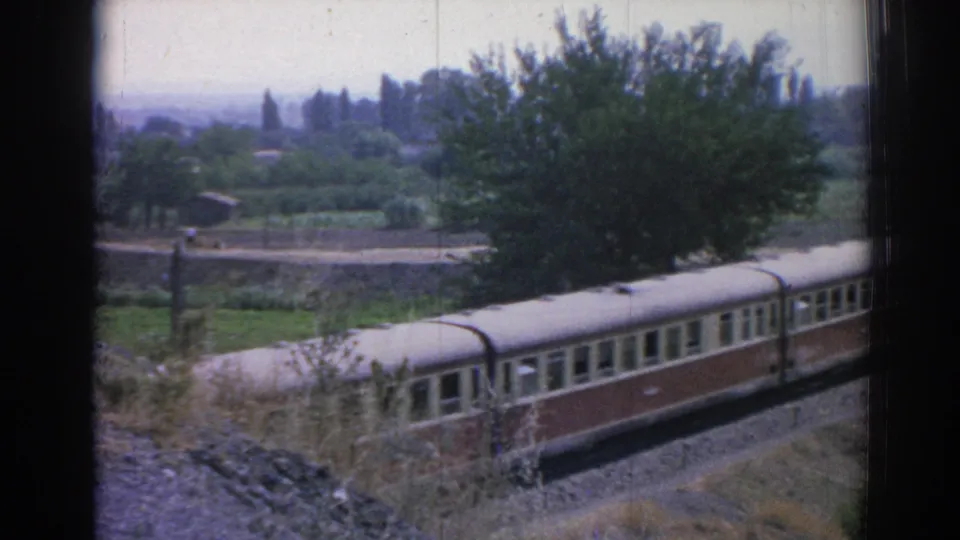 1962 Izmir-area frame showing the train moving across the lower edge of a rural landscape with a large tree and distant greenery.