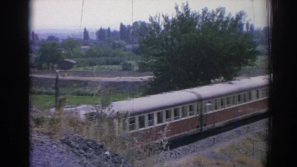 1962 Izmir-area home-movie frame showing a passenger railcar beside fields, trees, and distant hills.
