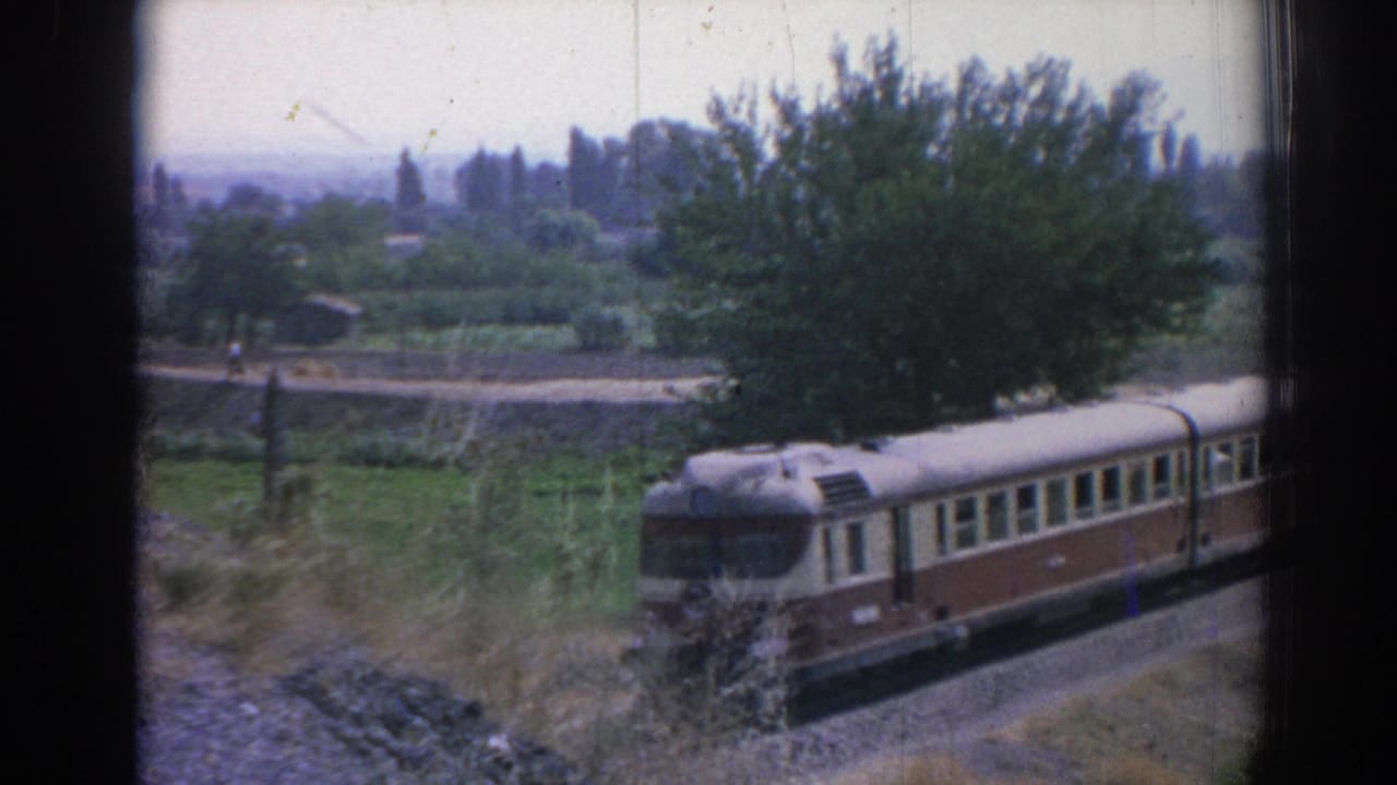 Front of a passenger railcar moving past fields and trees.