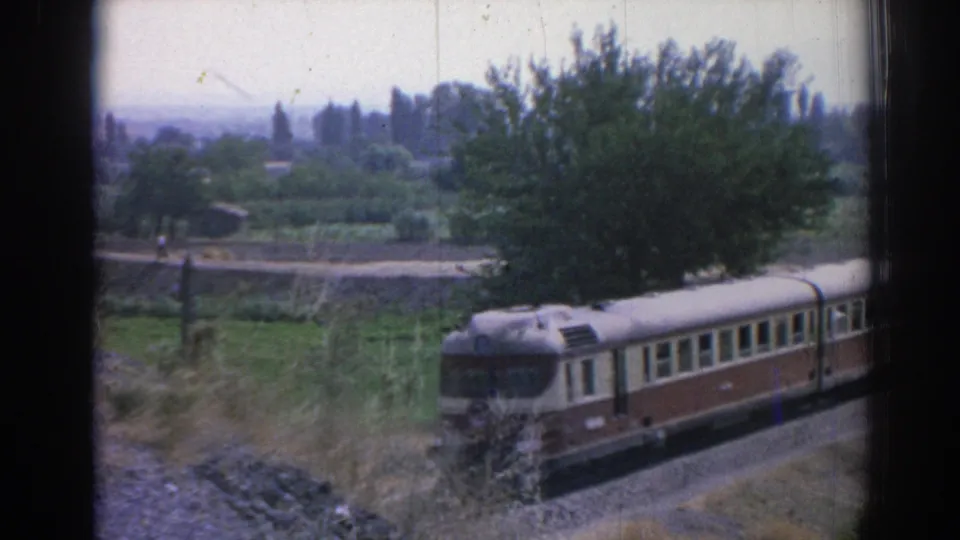 1962 Izmir-area 8mm view of a passenger railcar traveling beside cultivated fields and roadside trees.