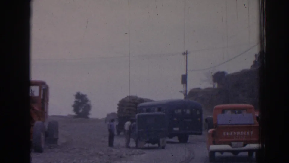 1962 Izmir 8mm frame with pedestrians near buses, stacked roadside material, utility poles, and an orange Chevrolet pickup.