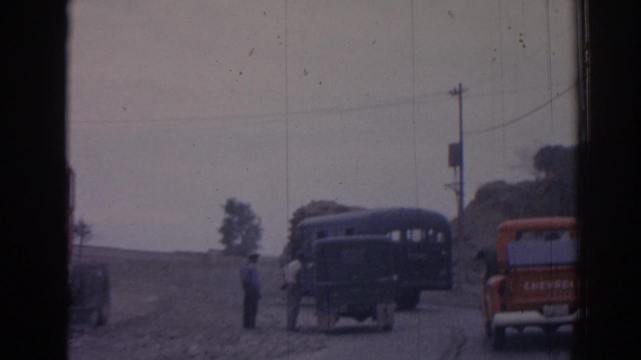 Rural road with a dark bus, red pickup, uniformed men, and window-frame bars in front.