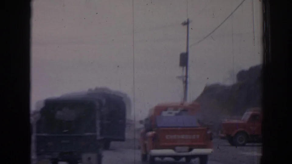 Dark bus and red Chevrolet pickup appear on a rural road outside Izmir, with utility poles, dust, and window-frame bars visible.
