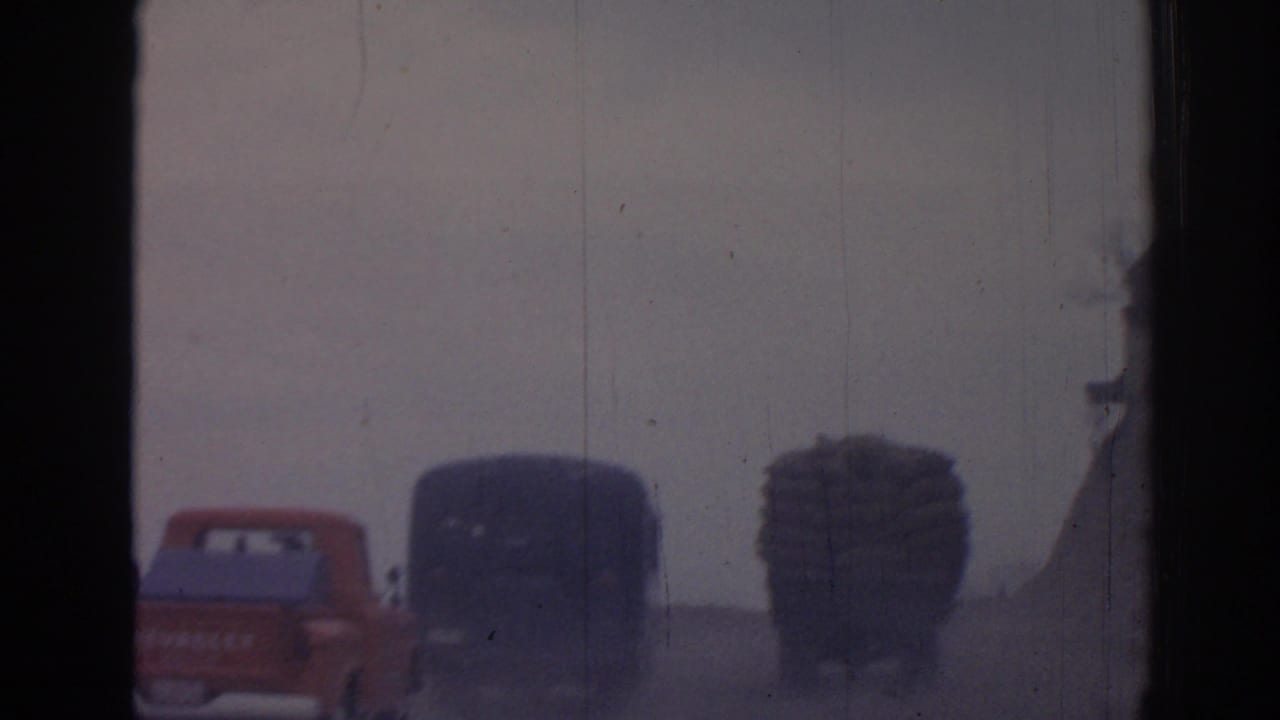 Red Chevrolet pickup and dark trucks seen through dark frame edges on a hazy road.