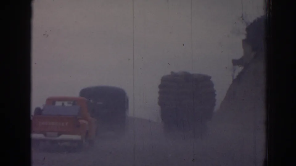 1962 Izmir home-movie frame showing the pickup and trucks receding through a soft, dusty roadside view.