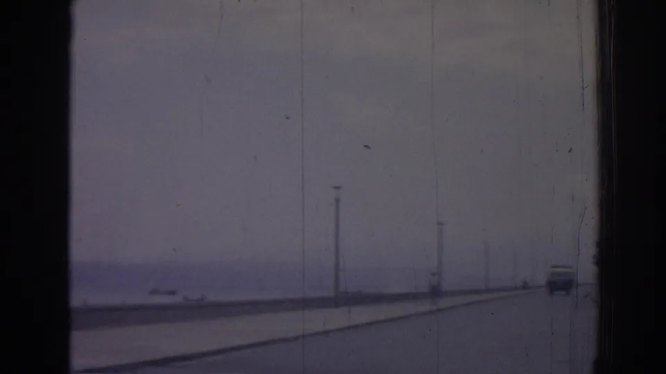 Sparse coastal roadway in Izmir, Turkey, with the sea to the left, lamp posts along the shore, and a distant car ahead.
