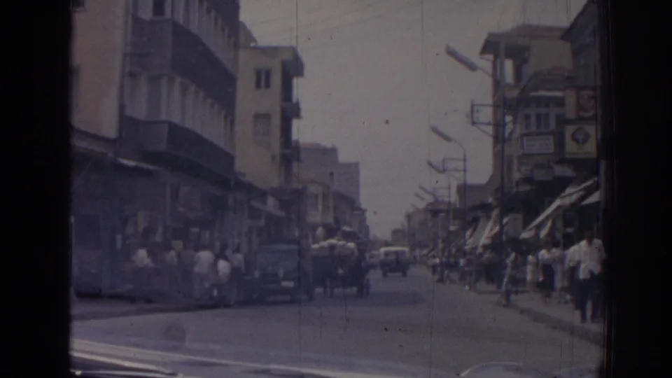 1962 Izmir street scene with pedestrians on sidewalks, cars in the road, shopfronts, awnings, and multi-story buildings.