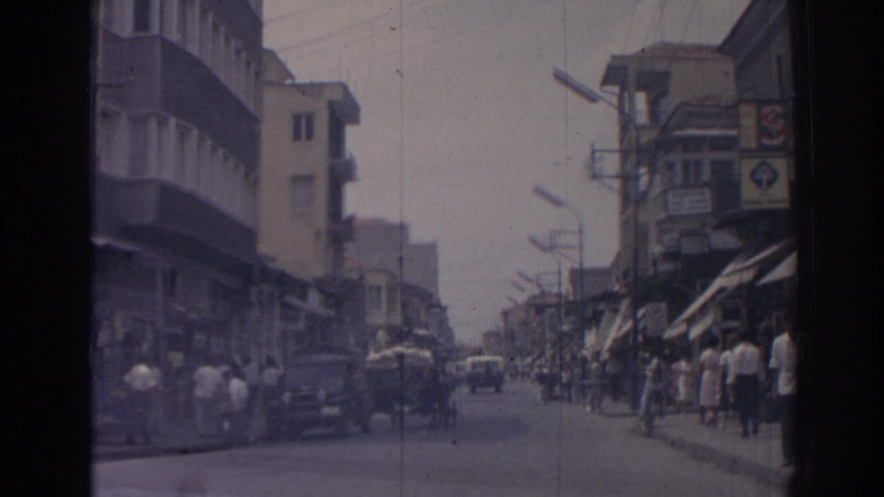 1962 Izmir street view with pedestrians near storefront awnings, classic cars, balconies, and a cart sharing the road.