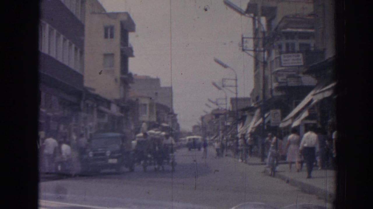 Street scene with pedestrians on sidewalks, cars in the road, awnings, balconies, and signs.