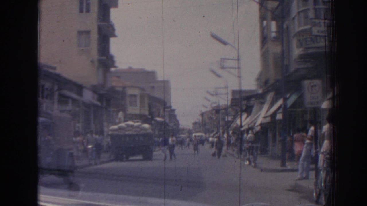 1962 Izmir street seen from a moving car, with pedestrians along storefronts and a sack-loaded truck in the road.