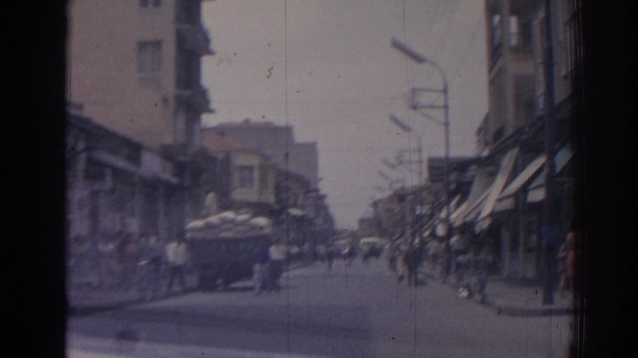 Busy street with a loaded truck ahead, pedestrians on both sides, and awnings along storefronts.