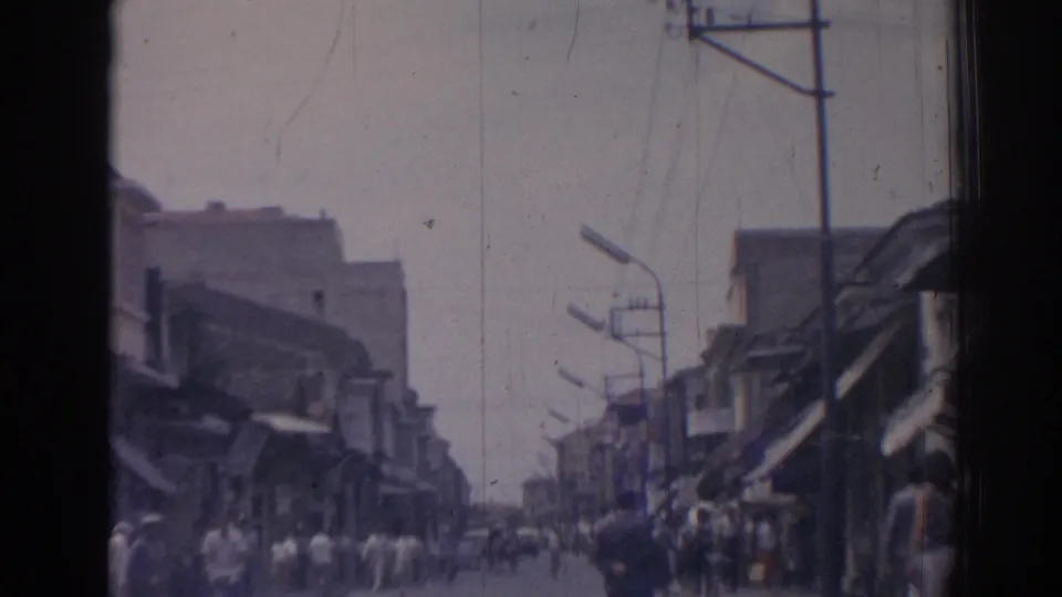 Soft 8mm frame looking down an Izmir street, with pedestrians gathered near shops and overhead poles receding into the distance.