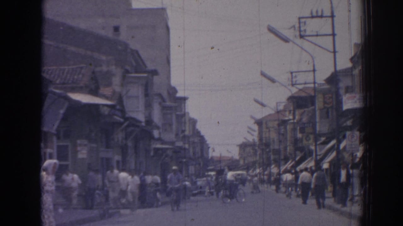 1962 Izmir street view with pedestrians moving past shop awnings, bicycles, streetlamps, and low-rise commercial buildings.