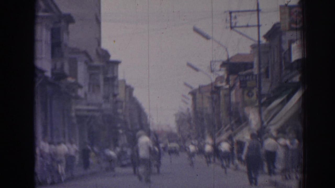 Blurred commercial street with pedestrians, bicycles, awnings, and buildings.