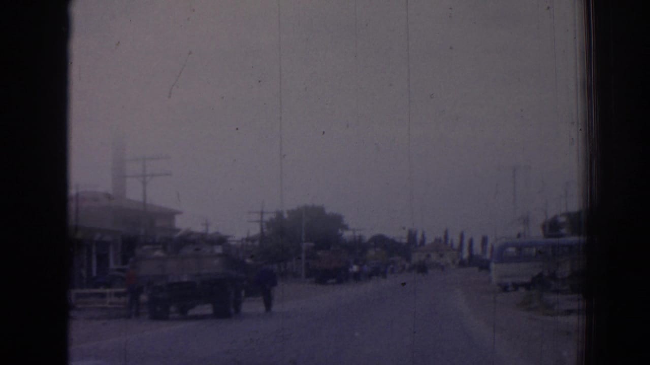 Street viewed from a moving vehicle with trucks, pedestrians, utility poles, and a minaret at left.