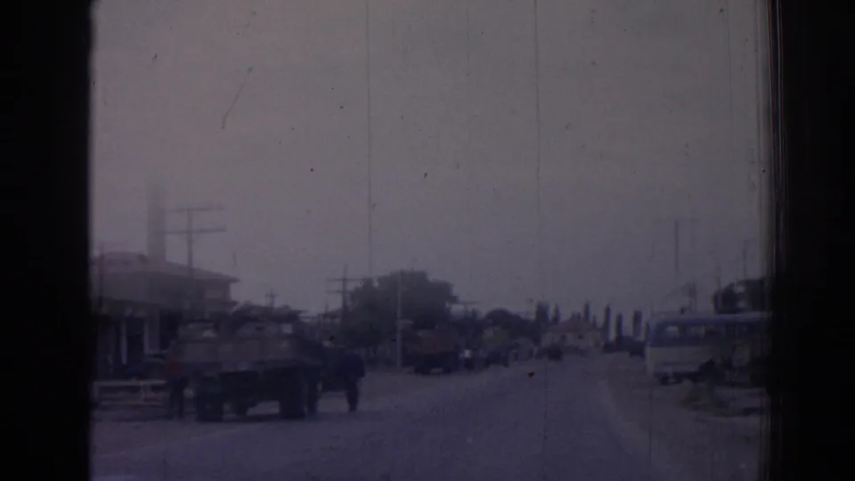 1962 Izmir street view from a moving vehicle, showing trucks, pedestrians, roadside buildings, utility poles, and a mosque minaret.