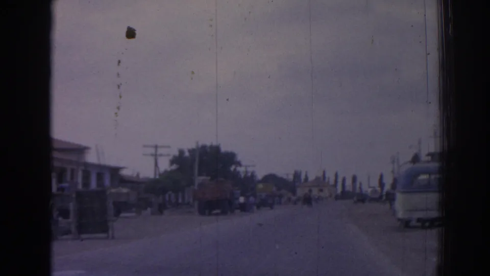 1962 Izmir roadway with pedestrians and vehicles moving through a broad street lined by utility poles and low buildings.