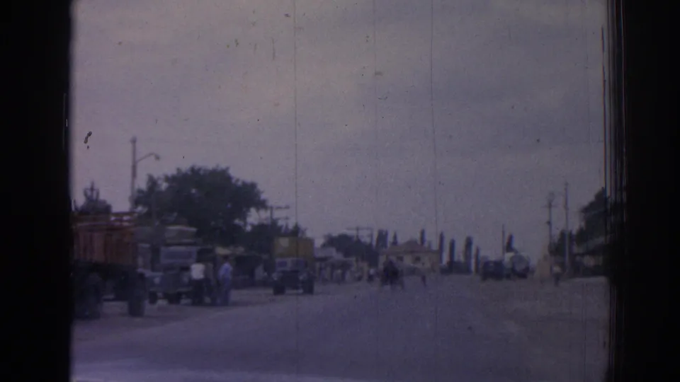 1962 Izmir forward street view with pedestrians, older trucks, roadside trees, utility poles, and low buildings in the distance.
