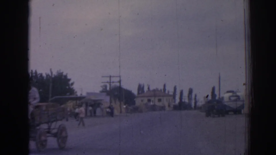 The 1962 Izmir street scene continues with a horse carriage near the left edge, pedestrians crossing, classic cars, poles, trees, and roadside buildings.