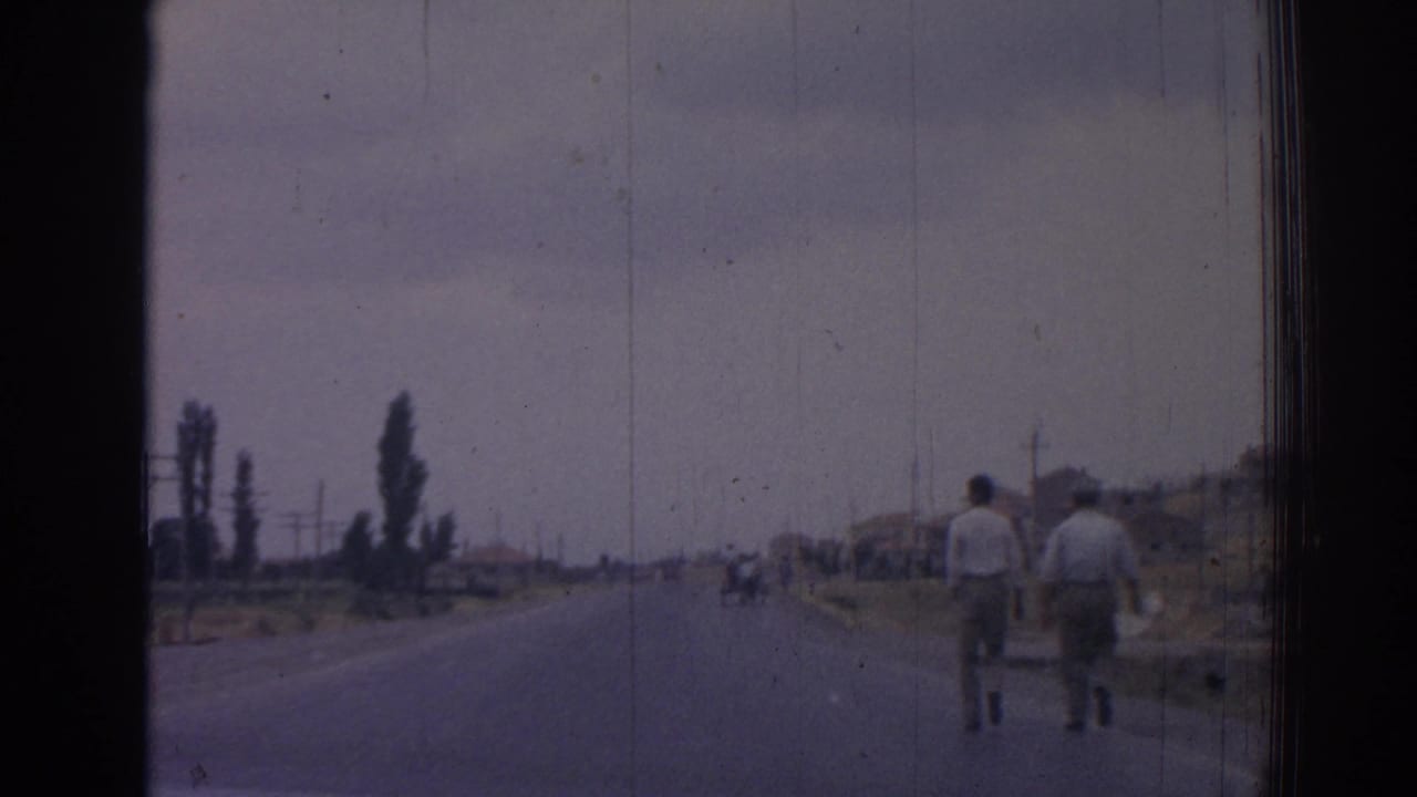 Men walk near the right side of a road while distant figures and a cart appear ahead.
