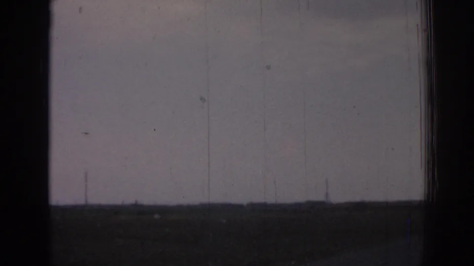 This 1962 Izmir home-movie frame shows open roadside landscape, a low horizon, faint utility poles, and aged 8mm film texture.