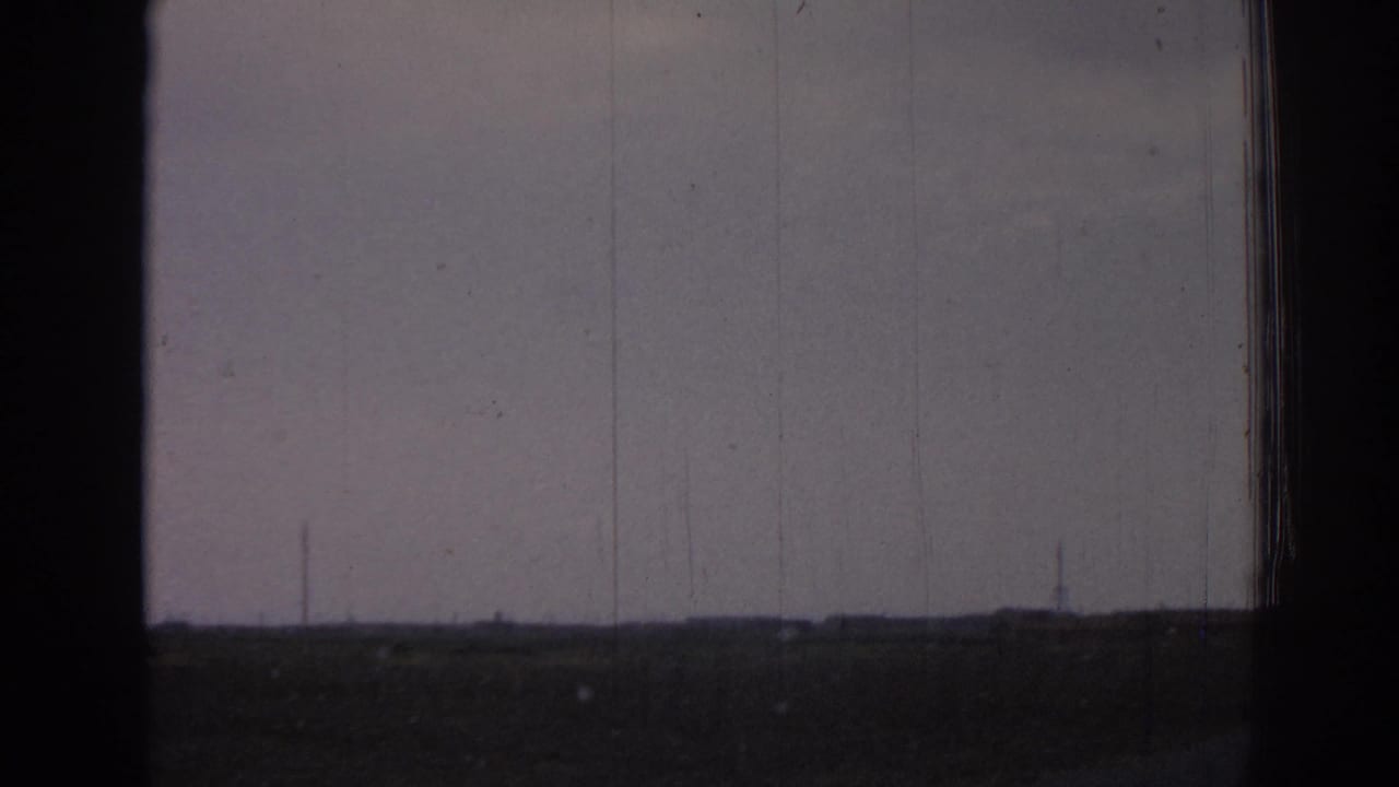 Flat rural horizon seen through dark frame borders with distant utility towers under a pale sky.