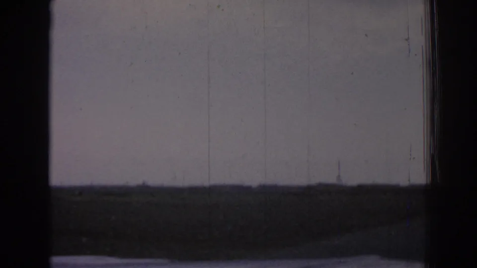 Passenger-view 8mm frame near Izmir with distant electrical towers across a low, open rural horizon.