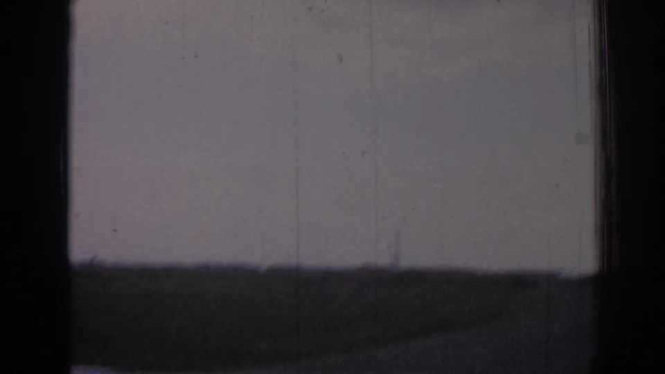 Faded 8mm view of open land near Izmir, with a low horizon and faint structures seen from a moving vehicle.