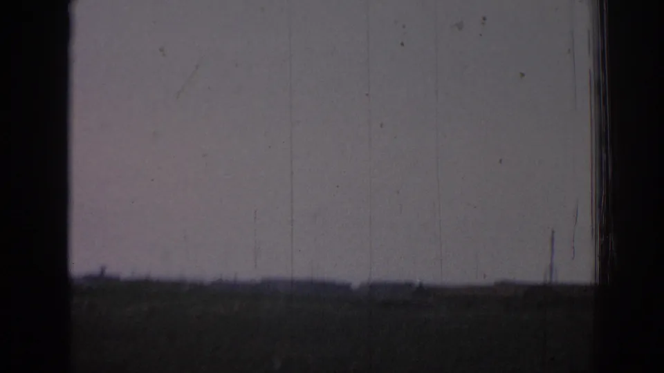 1962 8mm frame from Izmir showing open rural land, a distant tower, and heavy dark frame edging.