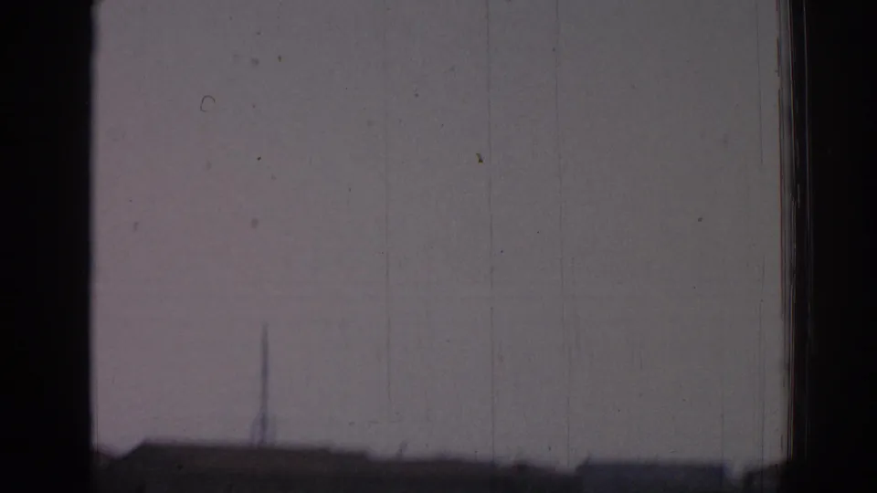 Soft 1962 Izmir home-movie frame seen through a window, with dark mullions and a faint exterior skyline beyond.