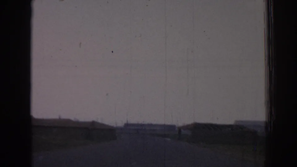 Through-window 1962 Izmir frame with a dark foreground frame, open roadway, and low distant buildings under faded color.