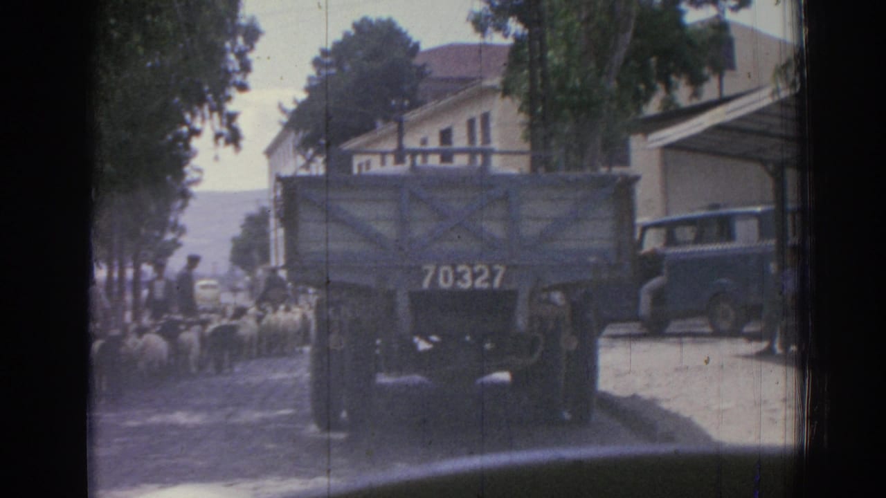 1962 Izmir home-movie frame showing sheep on a shaded town street near a canvas-covered truck marked 70327 and low buildings.