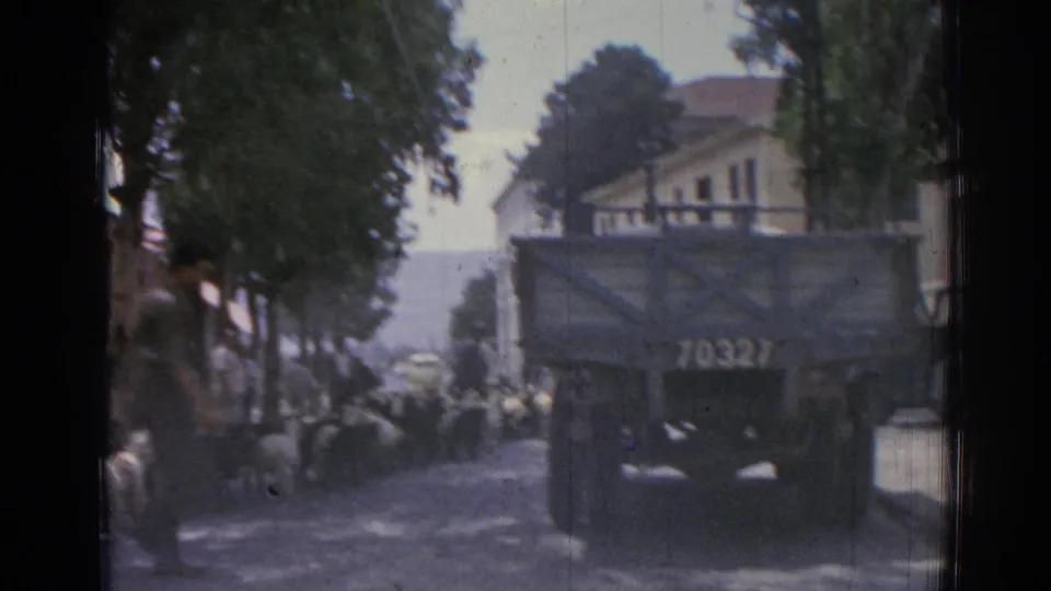 1962 Izmir street view with a canvas-covered truck marked 70327, sheep in the road, trees, buildings, and distant hills.