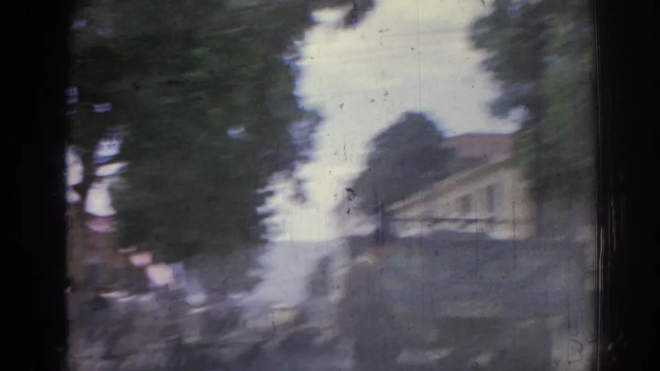 Motion-blurred 8mm frame from Izmir, showing trees, a pale building, and street edges during a quick handheld camera move.