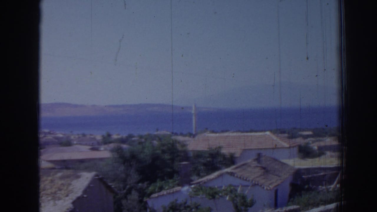 1962 Izmir frame with low buildings and trees in the foreground, the sea and mountains beyond, and a slim minaret near center right.