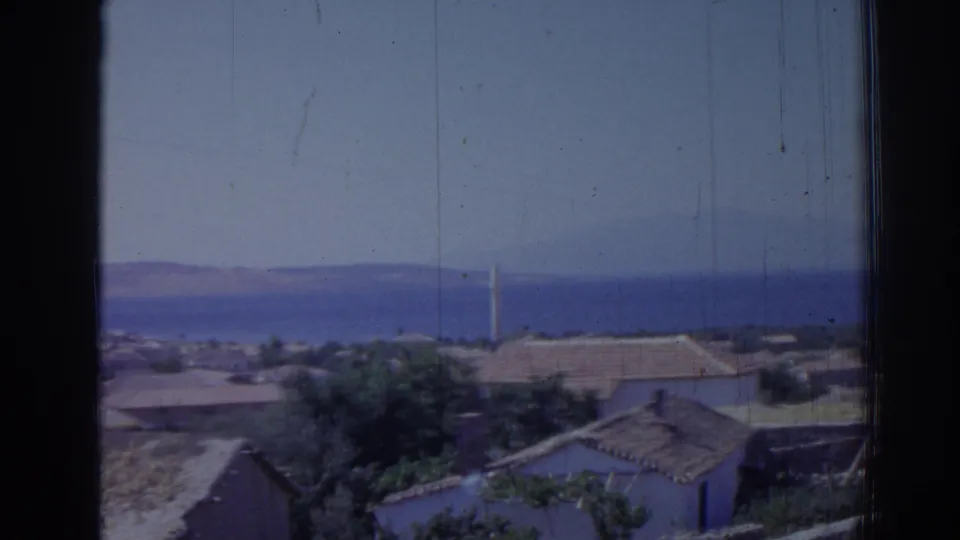 1962 Izmir frame with low buildings and trees in the foreground, the sea and mountains beyond, and a slim minaret near center right.