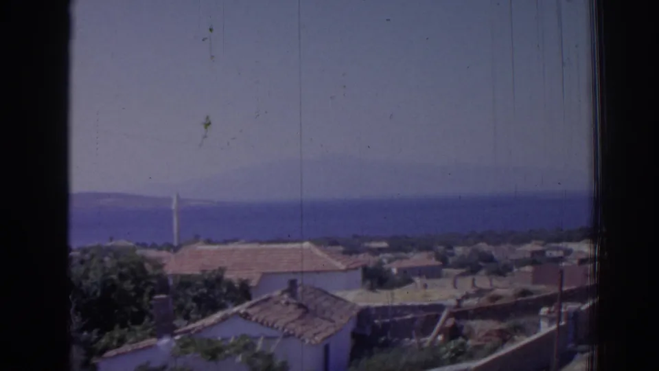 Late frame of the 1962 Izmir view, showing terracotta roofs, white walls, greenery, sea, distant hills, and a minaret through visible film wear.