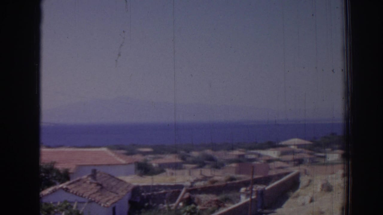 Village rooftops, pale ground, and sea horizon framed by dark vertical bars.