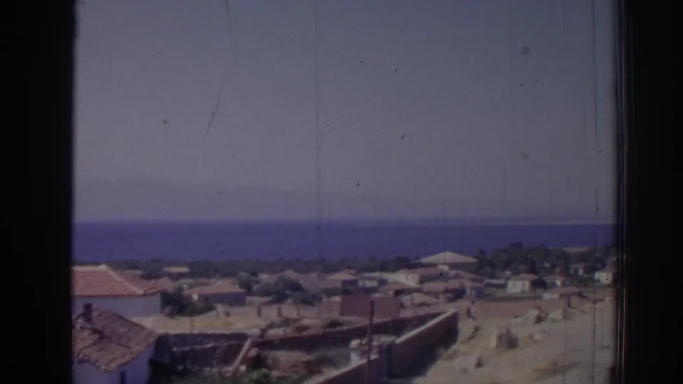 1962 Izmir coastal view showing village roofs, open ground, distant water, hazy sky, and visible film scratches.