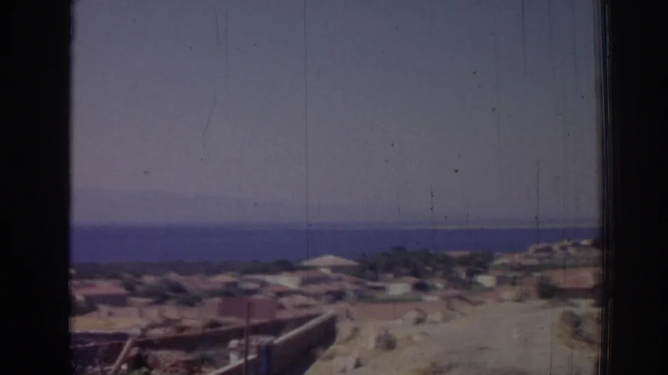 1962 8mm view over a hillside coastal area in Izmir, Turkey, with low buildings and the sea on the horizon.